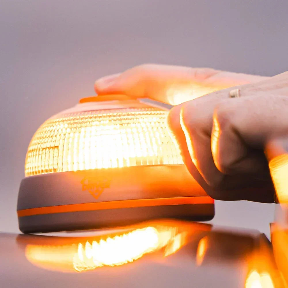 Mano agarrando baliza LED naranja encendida sobre superficie reflectante para seguridad vial