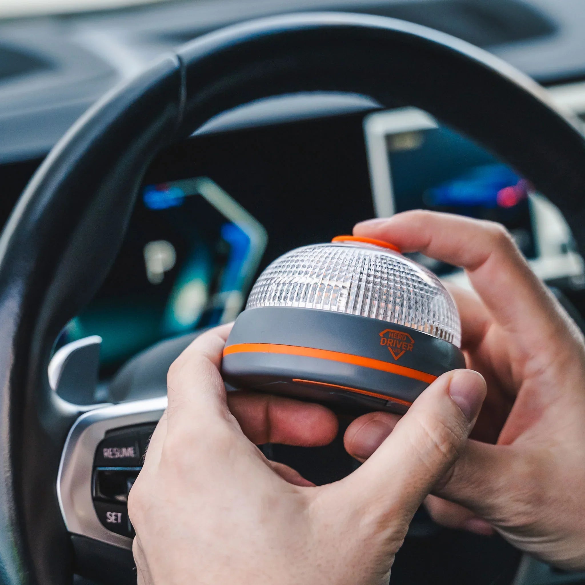 Manos sosteniendo una baliza LED certificada dentro de un coche con volante y panel digital
