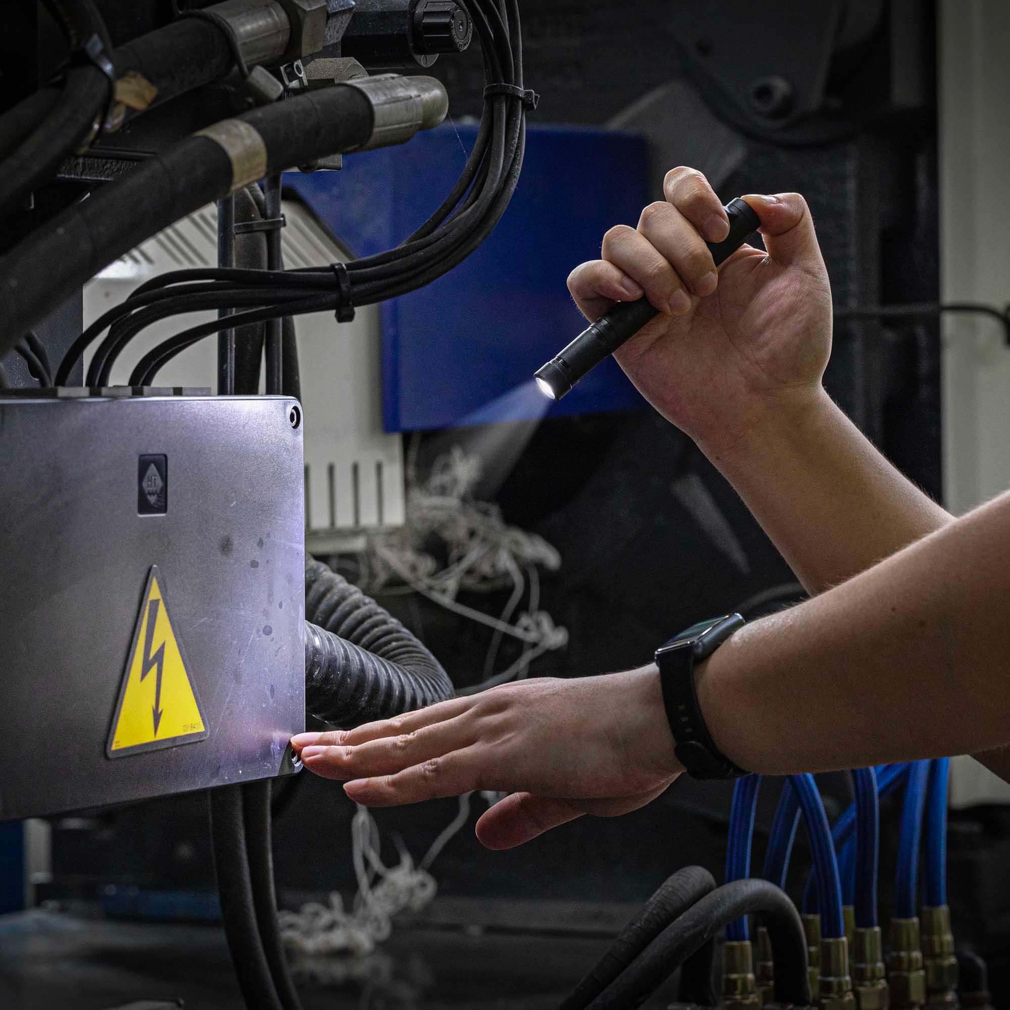Mano con linterna LED revisando caja eléctrica con cables y señal de peligro eléctrico