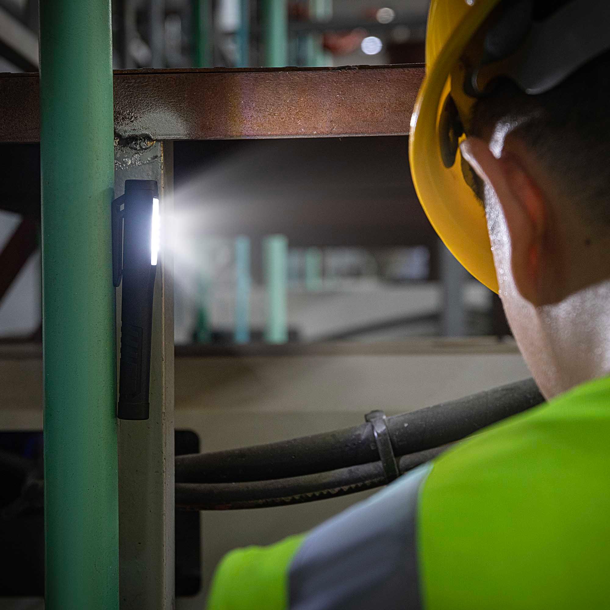 Trabajador industrial con casco amarillo usando linterna LED magnética en estructura metálica