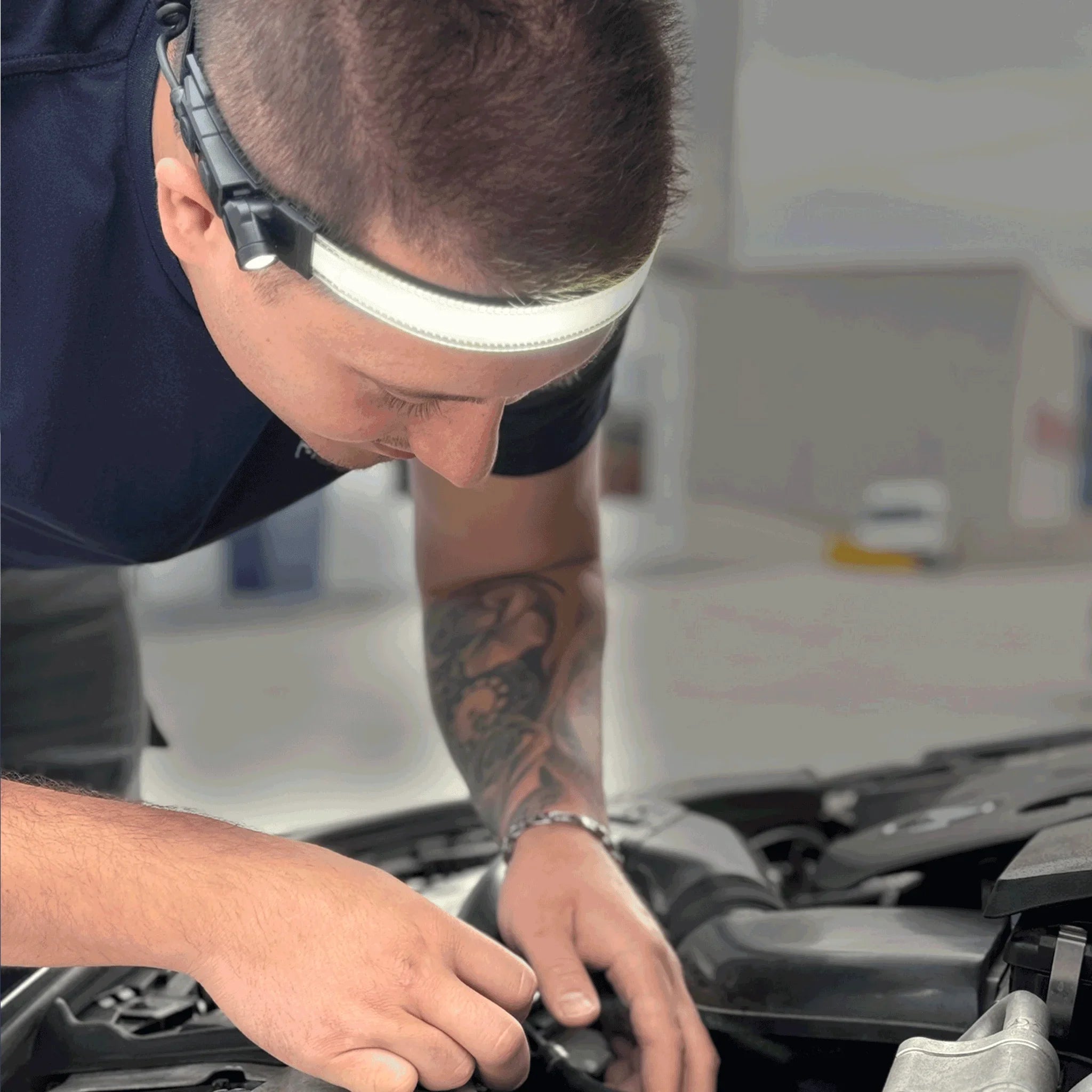 Hombre con lámpara frontal LED inspeccionando el motor de un coche, reparación y mantenimiento automotriz