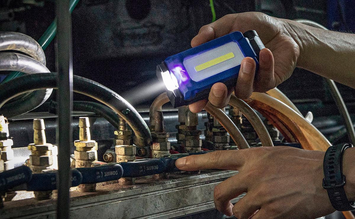 Manos sosteniendo foco de trabajo LED azul inspeccionando tuberías metálicas y conexiones