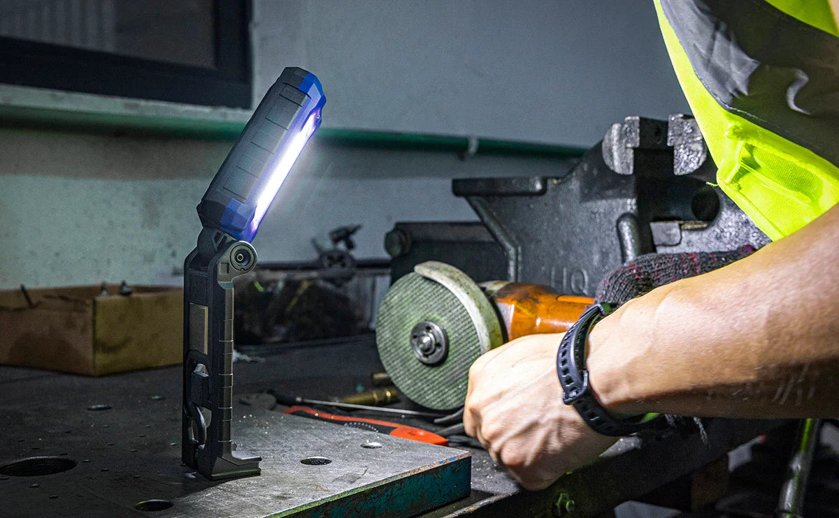 Baliza LED azul encendida sobre banco de trabajo metálico en taller con trabajador usando herramienta