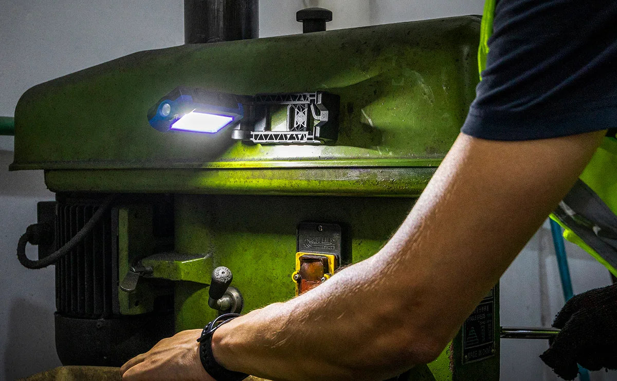 Baliza LED de trabajo iluminando maquinaria industrial verde mientras un operario ajusta controles