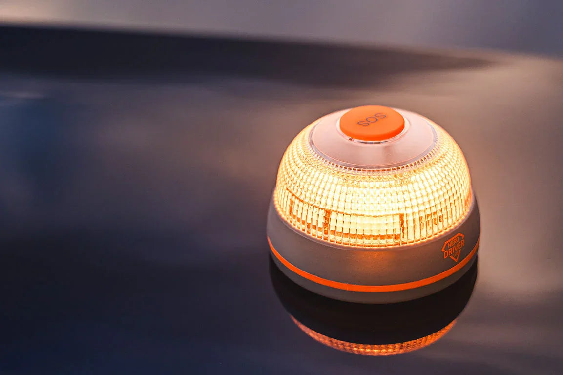 Baliza de emergencia con luz amarilla y botón SOS sobre superficie oscura, marca Hero Driver