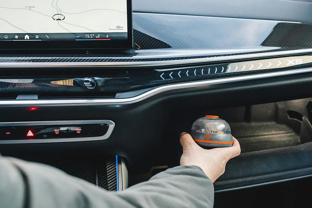 Mano sujetando baliza luminosa de emergencia dentro del tablero de un vehículo BMW X5 con pantalla de navegación y diseño moderno