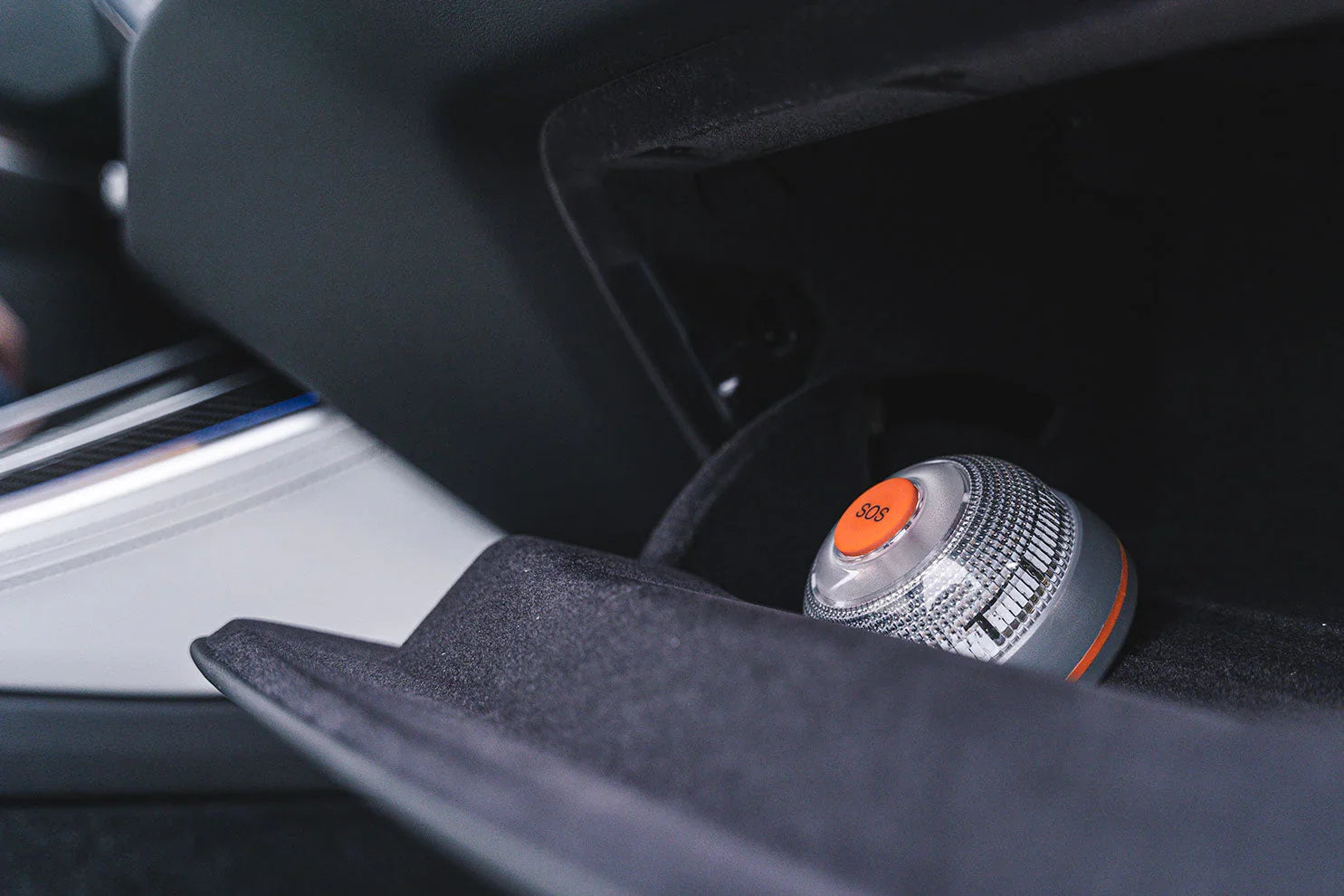 Botón SOS naranja en dispositivo de emergencia portátil dentro de guantera de coche