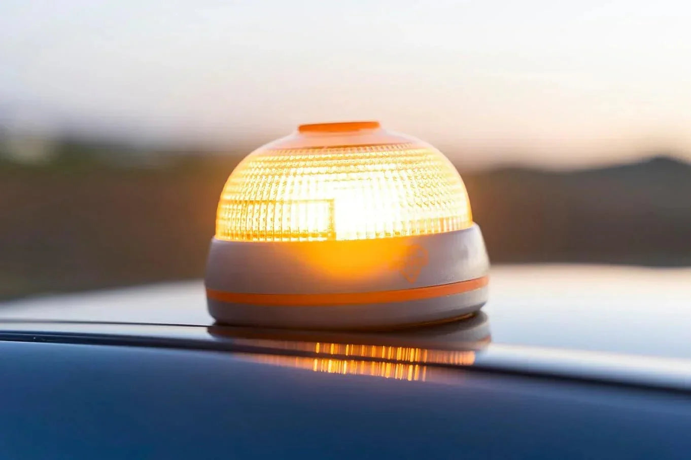 Baliza LED homologada DGT encendida sobre techo de coche al atardecer