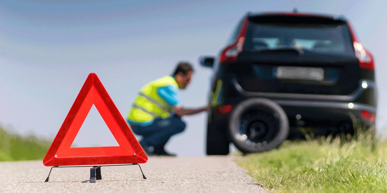 Triángulo de emergencia rojo en carretera con hombre revisando neumático pinchado en coche negro