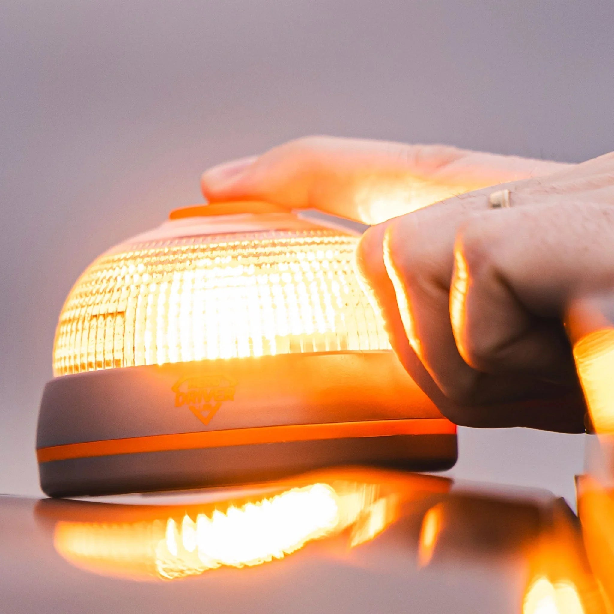 Mano activando una baliza V16 luminosa color naranja sobre un vehículo, luz encendida