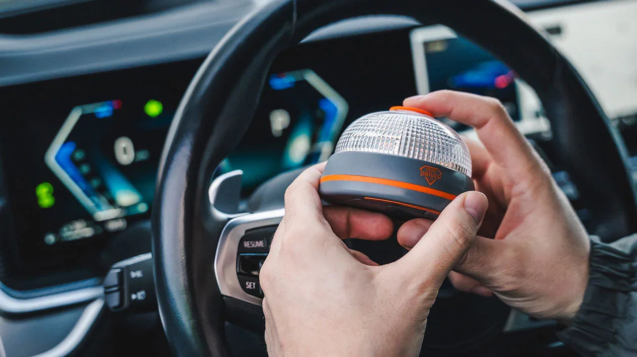 Manos sosteniendo luz de emergencia geolocalizada Hero Driver dentro de un coche con volante y panel digital