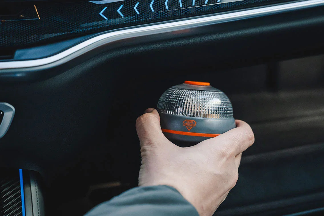 Mano sosteniendo luz de emergencia LED conectada y geolocalizada en interior de coche moderno