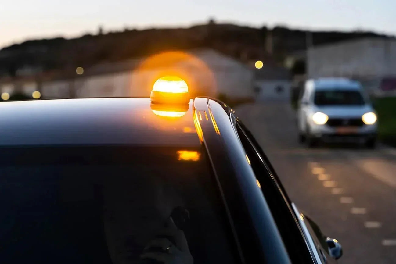Baliza luminosa LED amarilla sobre el techo de un coche negro al atardecer en una carretera
